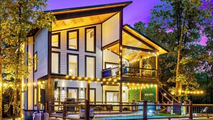 A modern two-story house with a large balcony, a swimming pool, and string lights. - 100% Kids & Adults LOVE this Cabin! Heated Pool, Espresso Bar, Playset, Pool Tbl (Broken Bow)