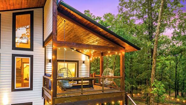 A two-story wooden cabin with a balcony, string lights, and a hot tub. - 100% Kids & Adults LOVE this Cabin! Heated Pool, Espresso Bar, Playset, Pool Tbl (Broken Bow)