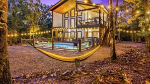A two-story cabin with a pool, surrounded by trees and string lights. - 100% Kids & Adults LOVE this Cabin! Heated Pool, Espresso Bar, Playset, Pool Tbl (Broken Bow)