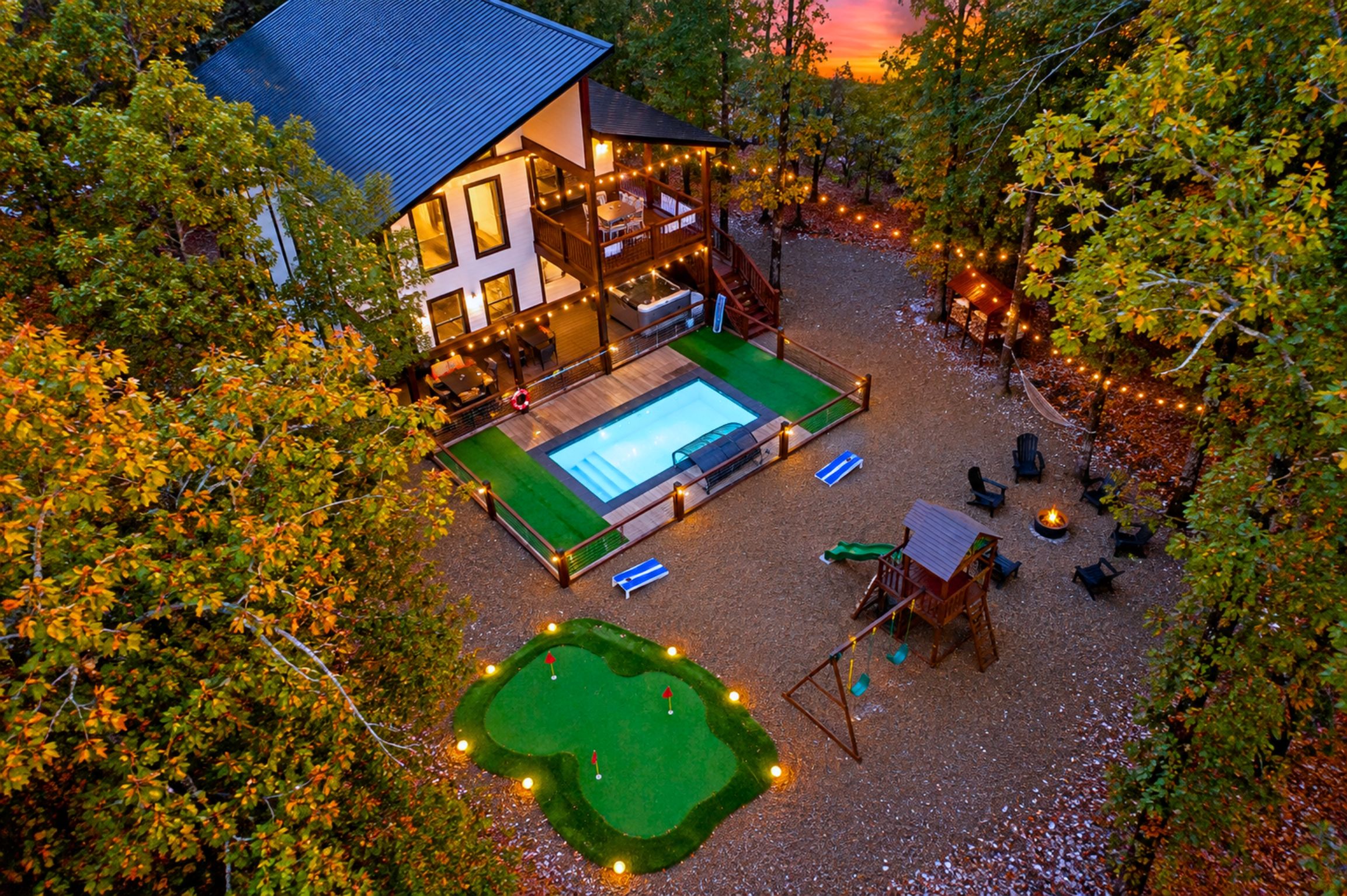 A two-story house with a swimming pool, deck chairs, and a fire pit.