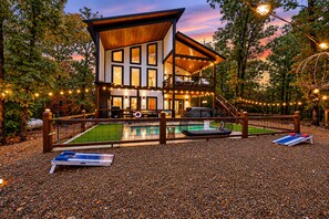 A two-story modern house with a pool, surrounded by a wooden fence and string lights. - 100% Kids & Adults LOVE this Cabin! Heated Pool, Espresso Bar, Playset, Pool Tbl (Broken Bow)