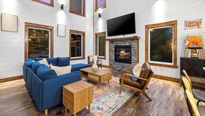 A living room with a fireplace, a sofa, a coffee table, and a TV mounted on the wall. - 100% Kids & Adults LOVE this Cabin! Heated Pool, Espresso Bar, Playset, Pool Tbl (Broken Bow)