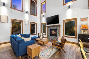 A living room with a fireplace, a sofa, a coffee table, and a TV mounted on the wall. - 100% Kids & Adults LOVE this Cabin! Heated Pool, Espresso Bar, Playset, Pool Tbl (Broken Bow)
