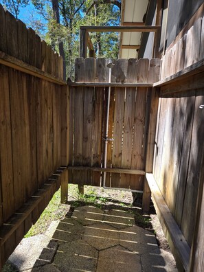 Une clôture en bois avec un portail, une zone pavée avec des carreaux hexagonaux et un ciel dégagé.
