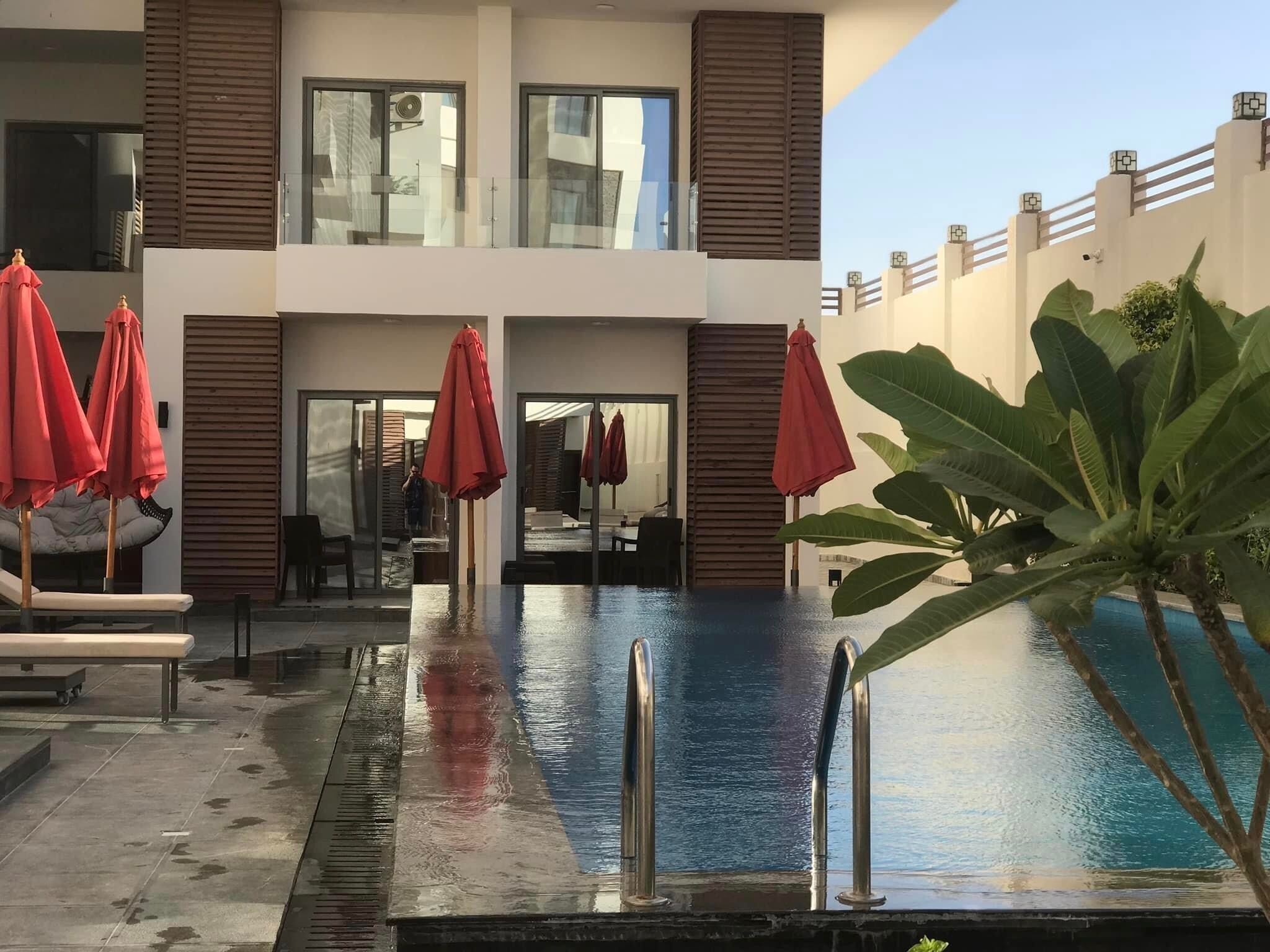 A modern hotel with a swimming pool, lounge chairs, and red umbrellas.