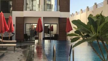 A modern hotel with a swimming pool, lounge chairs, and red umbrellas.
