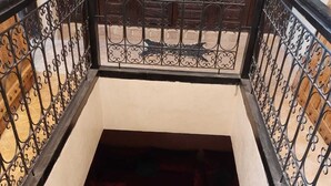 Un pequeño balcón cerrado con barandilla de hierro forjado, piso estampado y asientos con cojines rojos.