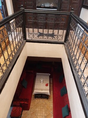 Un piccolo balcone chiuso con ringhiera in ferro battuto, pavimento decorato e sedute imbottite rosse.