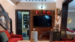 Una sala de estar con un televisor de pantalla plana grande, un conjunto de sofá, una mesa de centro y un adorno en la pared.
