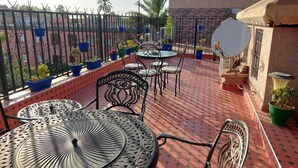 Una terraza en la azotea con mobiliario exterior, plantas en macetas y vistas a palmeras.