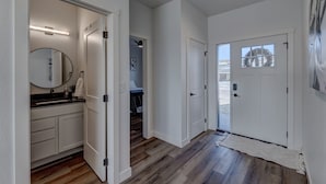 A hallway with wooden flooring, white walls, and a door leading to a bedroom. - Luxury Rapid City Home #2 (Rapid City)