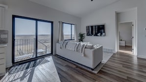 A spacious living room with a large window overlooking a beach, a ceiling fan, and a modern white sofa. - Luxury Rapid City Home #2 (Rapid City)