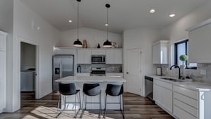 A modern kitchen with white cabinetry, a central island with bar stools, stainless steel appliances, and pendant lighting. - Luxury Rapid City Home #2 (Rapid City)