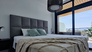 A modern bedroom with a large bed, a dark headboard, and a view of the outdoors through large windows.
