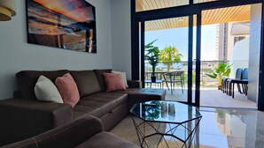 A modern living room with a leather sofa, a glass coffee table, and a large painting of a sunset.