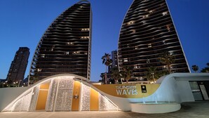A modern hotel with two prominent curved towers, a well-lit entrance, and a sign reading "Sunset Waves."
