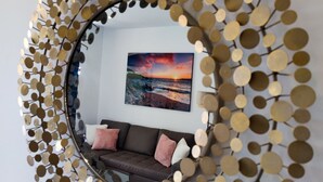 A living room with a round mirror, a brown sofa, and a framed picture of a sunset.