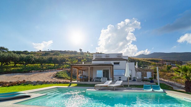 En modern villa med pool, utomhusmöbler och utsikt över det omgivande landskapet.