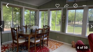 A dining area with a round table and six chairs, large windows with a view of a green landscape, and a patterned rug on the floor. - Large home on the 8th fairway of the Balboa Golf Course with decks and sunroom! (Hot Springs)