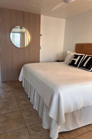 Ein Schlafzimmer mit einem großen Bett, einem runden Spiegel, einer Wand aus Holzleisten und einem Fliesenboden.
