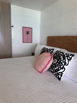 Una cama bien hecha con una cubierta blanca texturizada, un cabecero tejido y almohadones decorativos.