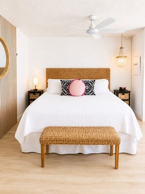 A bedroom with a bed, a ceiling fan, a bedside table with a lamp, and a wall-mounted light fixture.