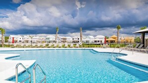 Una gran piscina al aire libre con varias pistas de natación, rodeada de sillas reclinables y palmeras.