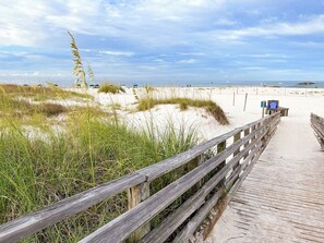 A wooden boardwalk leading to a sandy beach with dunes and grass.