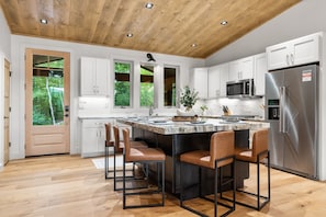 A modern kitchen with white cabinets, a stainless steel refrigerator, and a central island with bar stools.