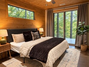 A bedroom with a large bed, two bedside lamps, a window with curtains, and a view of trees. - 4 Kings| No Bunks| Serene Views| Sauna| EV| Pets (Blue Ridge)