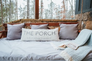 A bed with a stone wall and wooden beams, a pillow with text, and a book on the bed.