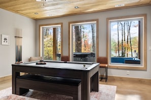 A pool table in a room with large windows, a ceiling fan, and a view of autumn trees.