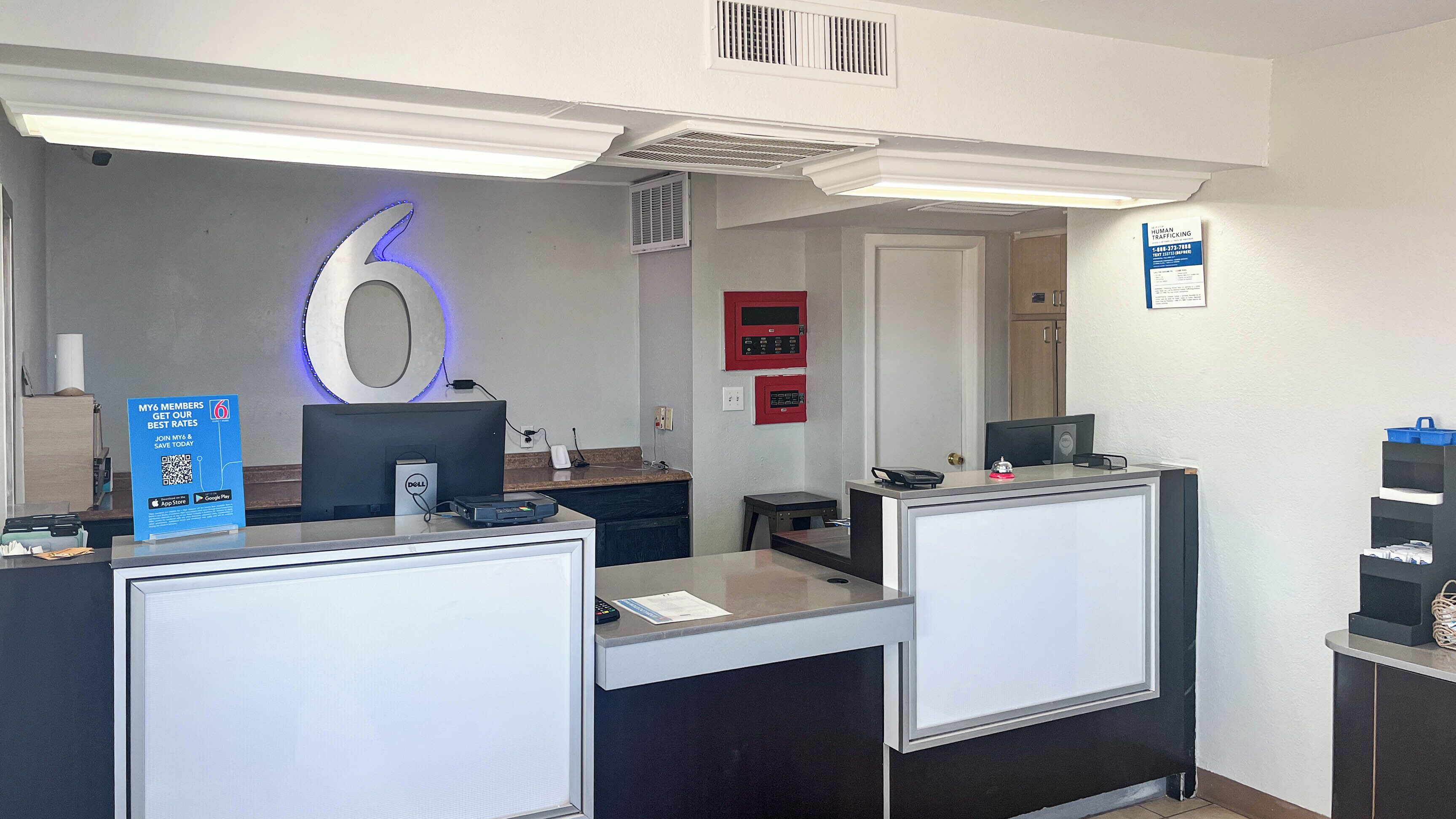 A reception desk with a large illuminated number 6, a sign promoting membership rates, and a fire alarm panel on the wall.