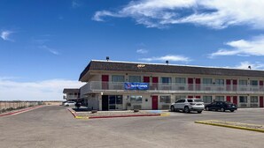 A motel with a '6 NOW OPEN' sign, a parking lot, and a clear blue sky.