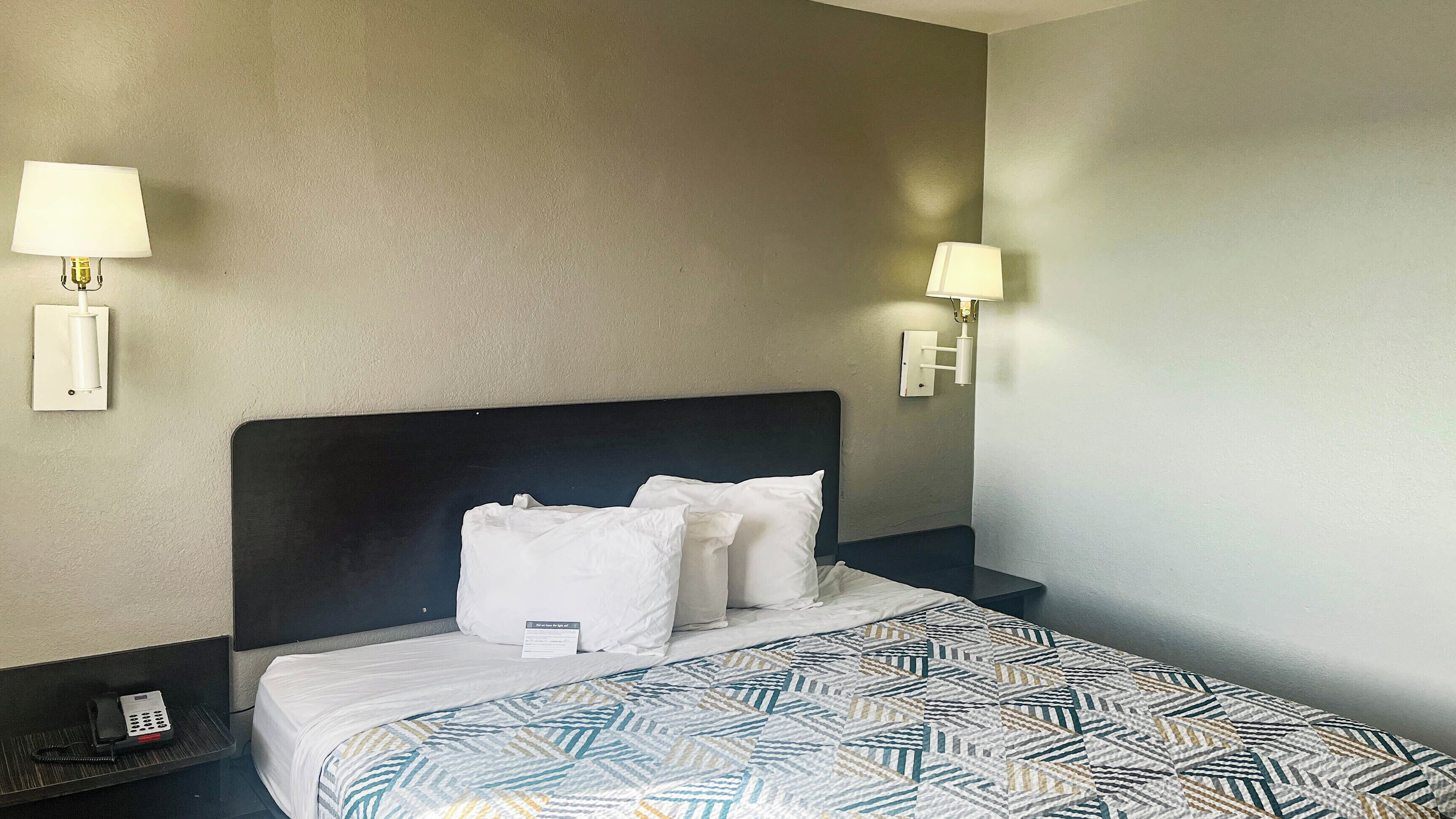 A hotel room with a bed, two bedside lamps, a telephone, and a patterned bedspread.