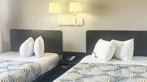 A hotel room with two beds, each with a headboard, a bedside table with a lamp, and a phone.