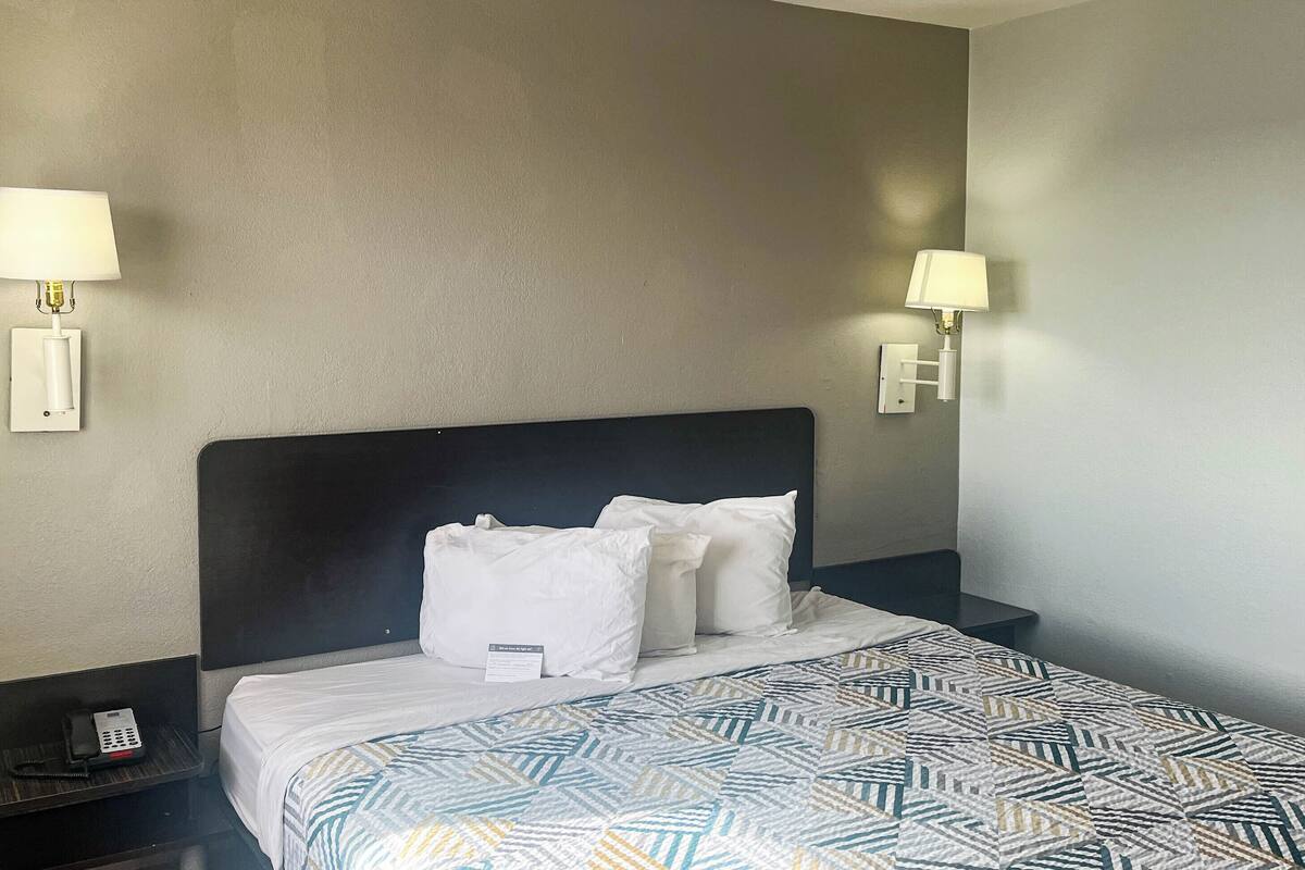 Ein Hotelzimmer mit Bett, zwei Nachttischlampen, einem Telefon auf dem Nachttisch und einer gemusterten Bettdecke.