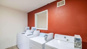 A laundry room with two white washing machines, a dryer, and a control panel.