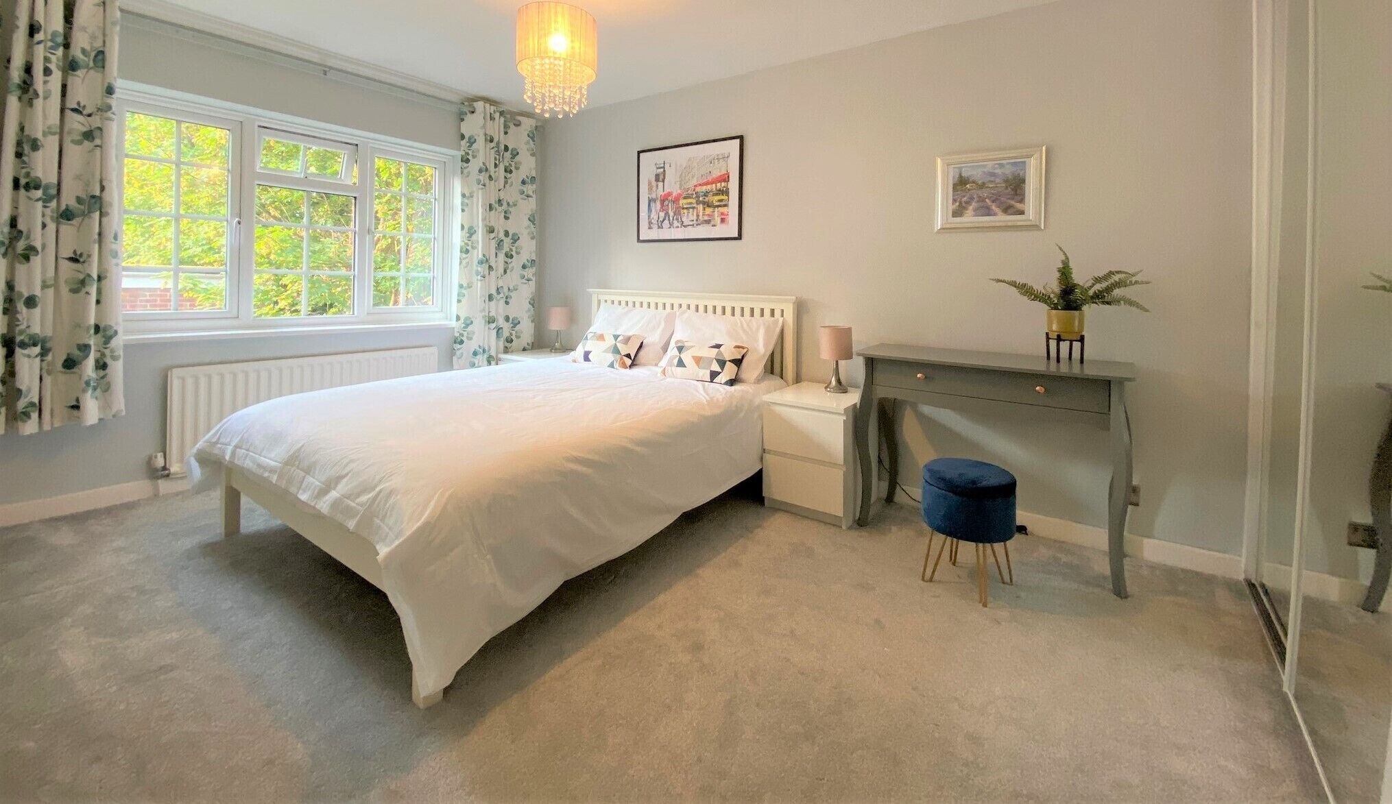 A bedroom with a bed, bedside table, lamp, desk, chair, and two framed pictures on the wall.