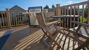 A wooden deck with a grill, chairs, and a table.