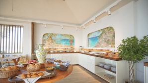 A breakfast buffet with various food items and a large painting of a coastal scene.