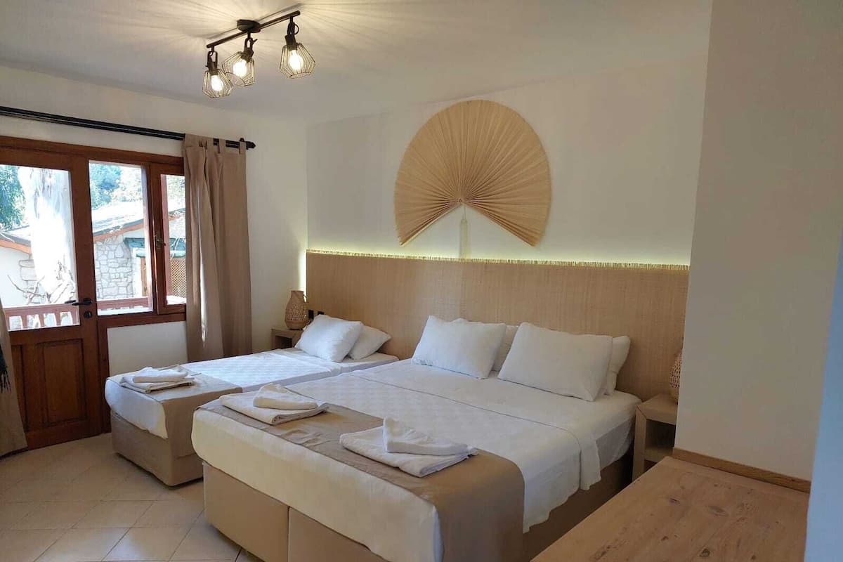 A hotel room with two beds, a large window with curtains, a wooden headboard, and a wall fan.