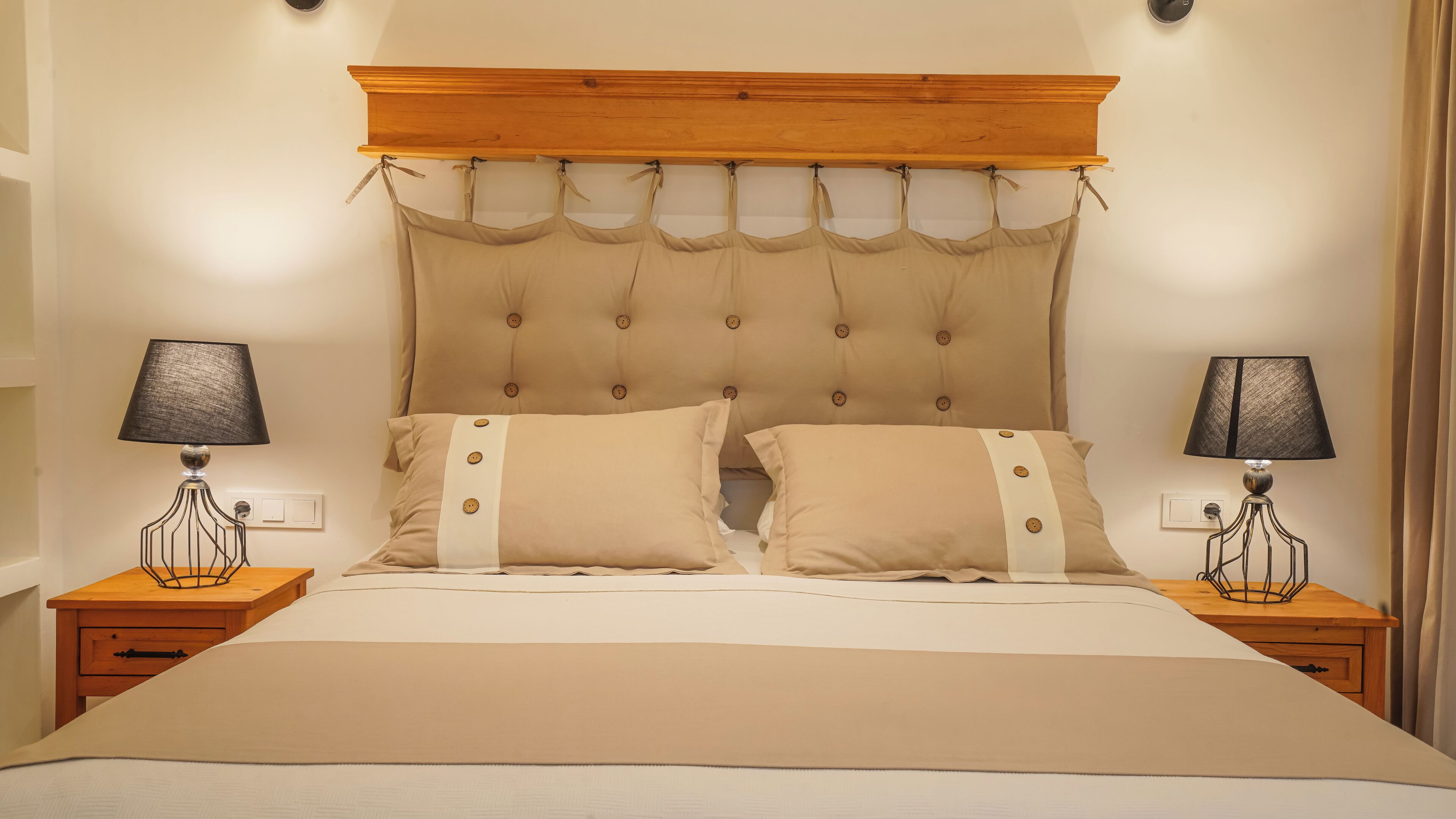 Una cama con cabecera de madera, dos mesitas de noche con lámparas y dos almohadas con botones.
