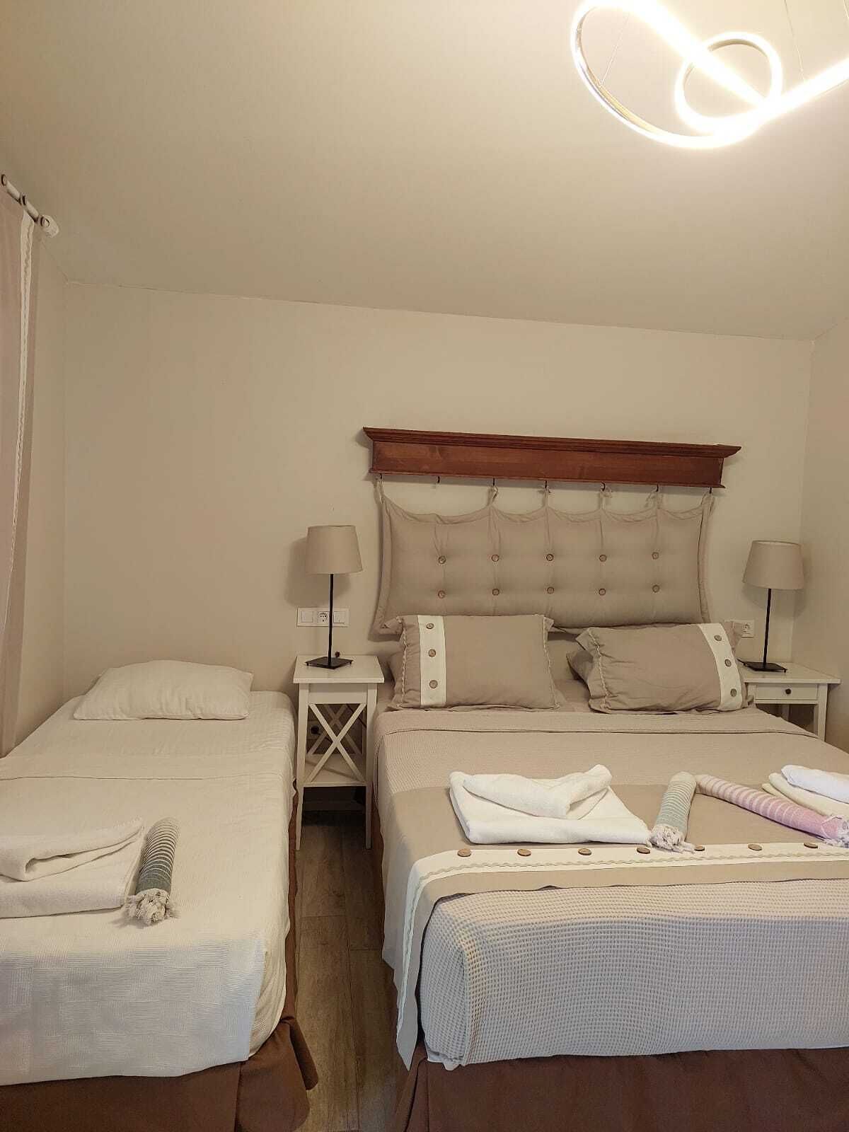 A hotel room with two beds, each with a headboard, bedside tables with lamps, and a large window with curtains.