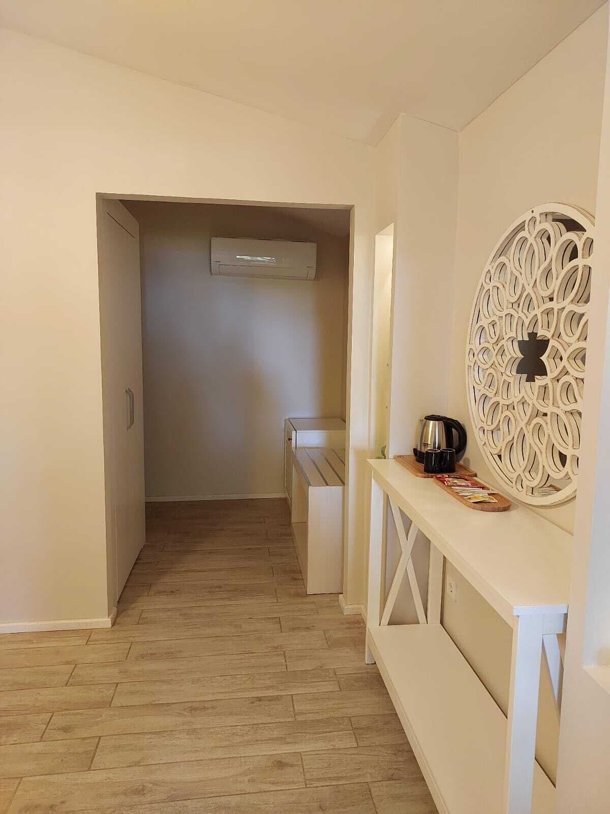 Un pasillo con suelo de madera, un banco blanco, un elemento decorativo en la pared y una cafetera sobre el banco.