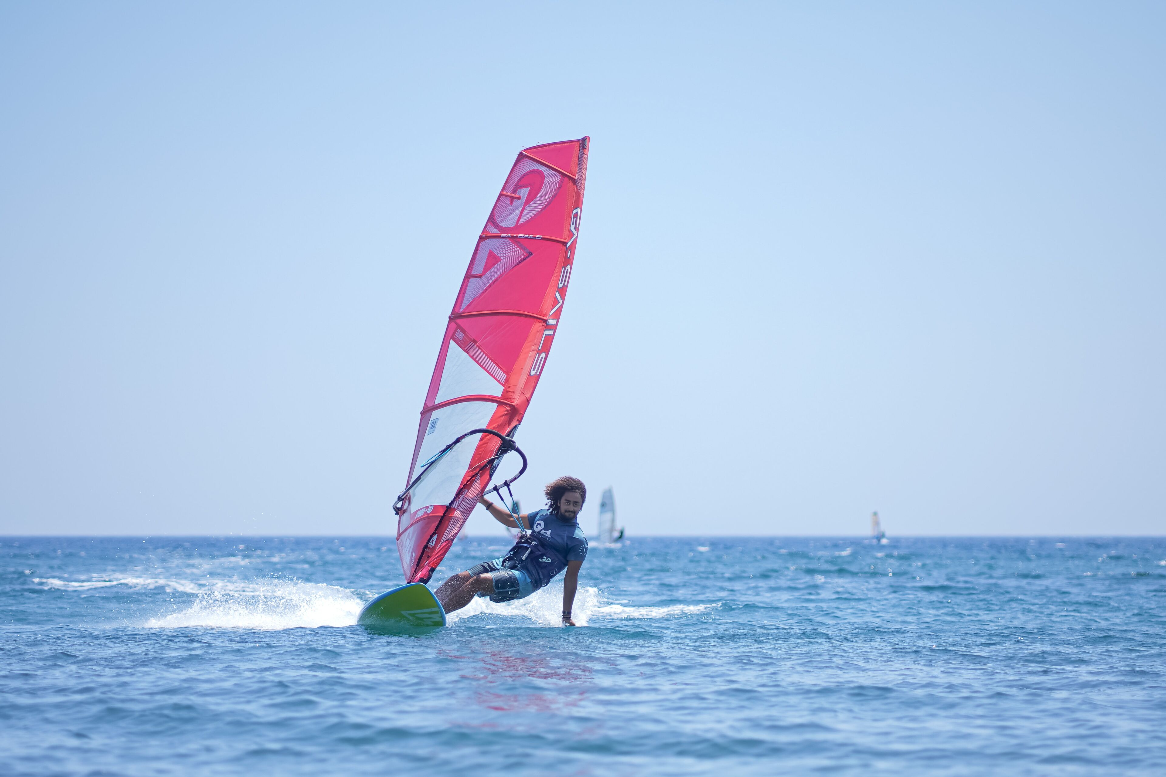 A person windsurfing on the water with a red sail.