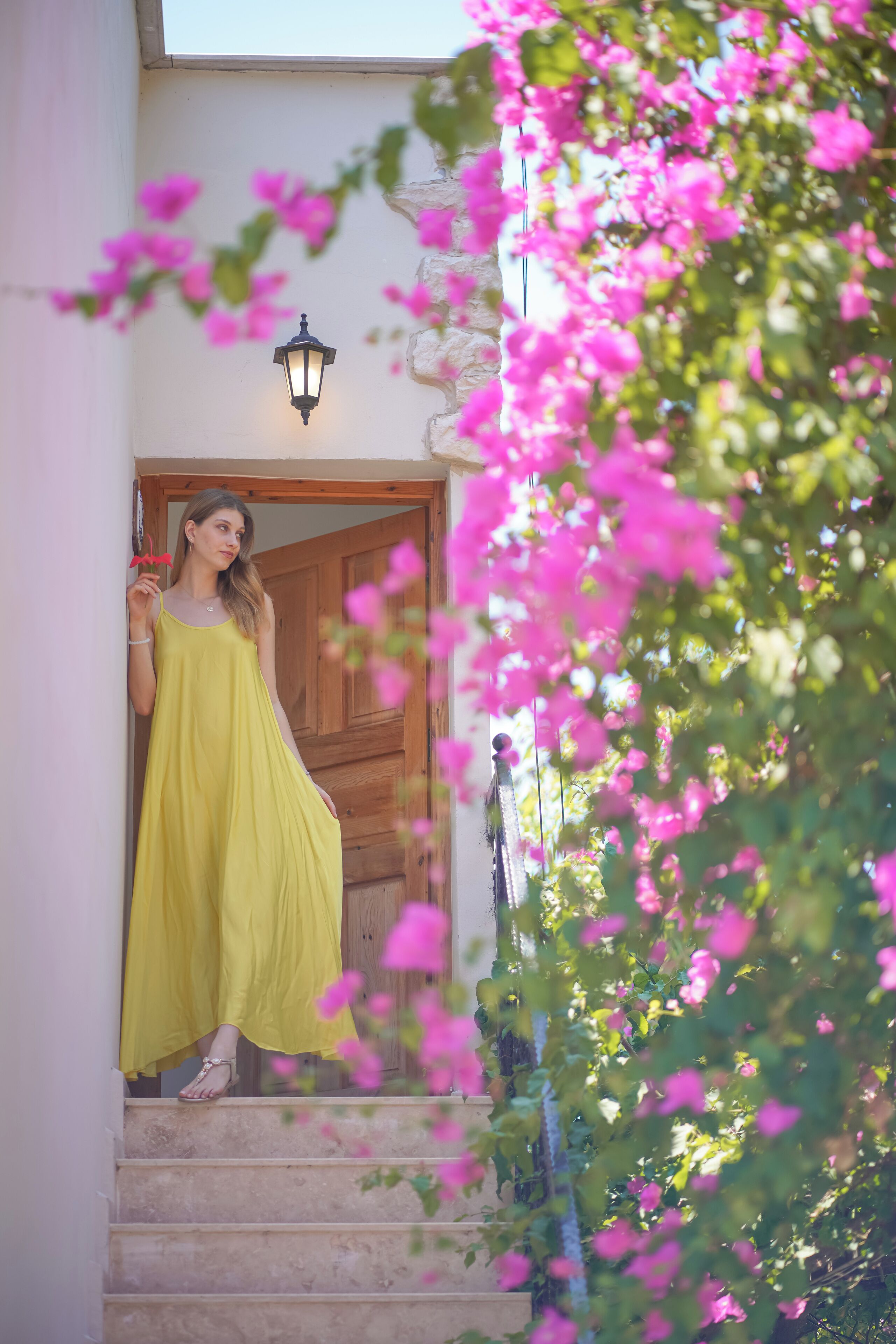 A person in a yellow dress standing on a staircase with a wooden door and a wall-mounted light fixture.