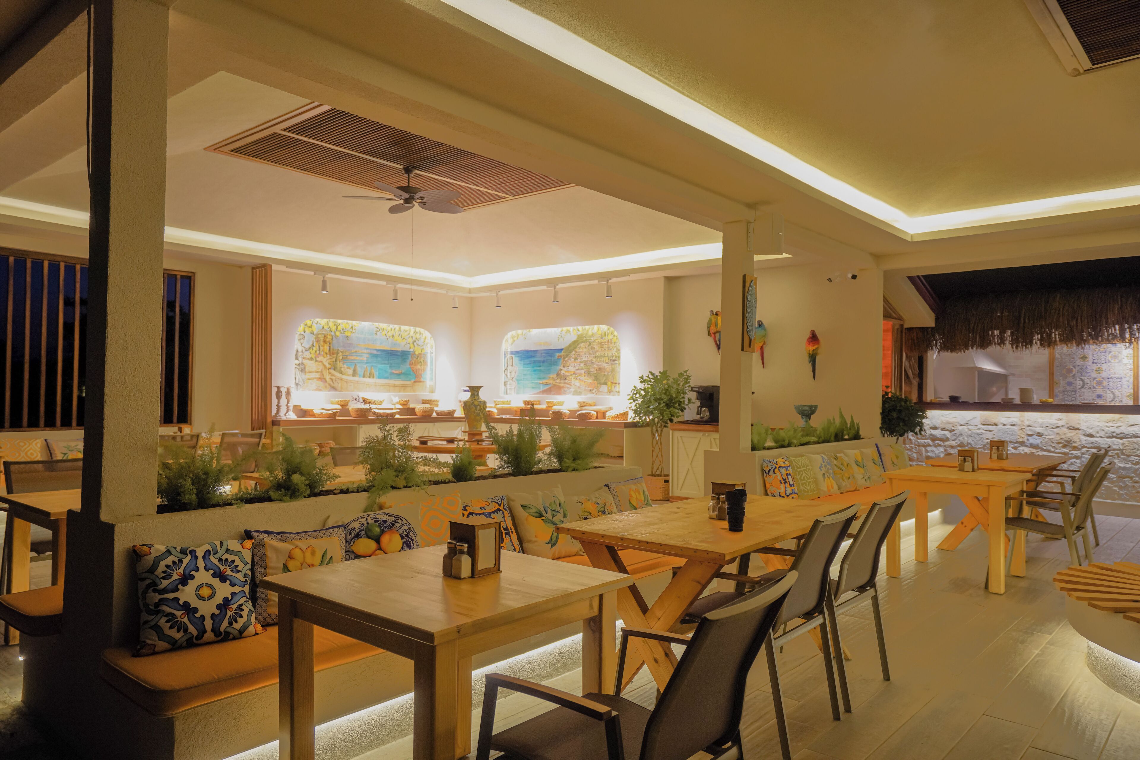 A spacious dining area with a long wooden table and multiple chairs, surrounded by cushioned seating and decorative pillows.