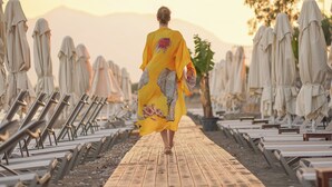 A person walking along a wooden pathway lined with beach chairs and umbrellas, with mountains in the background.