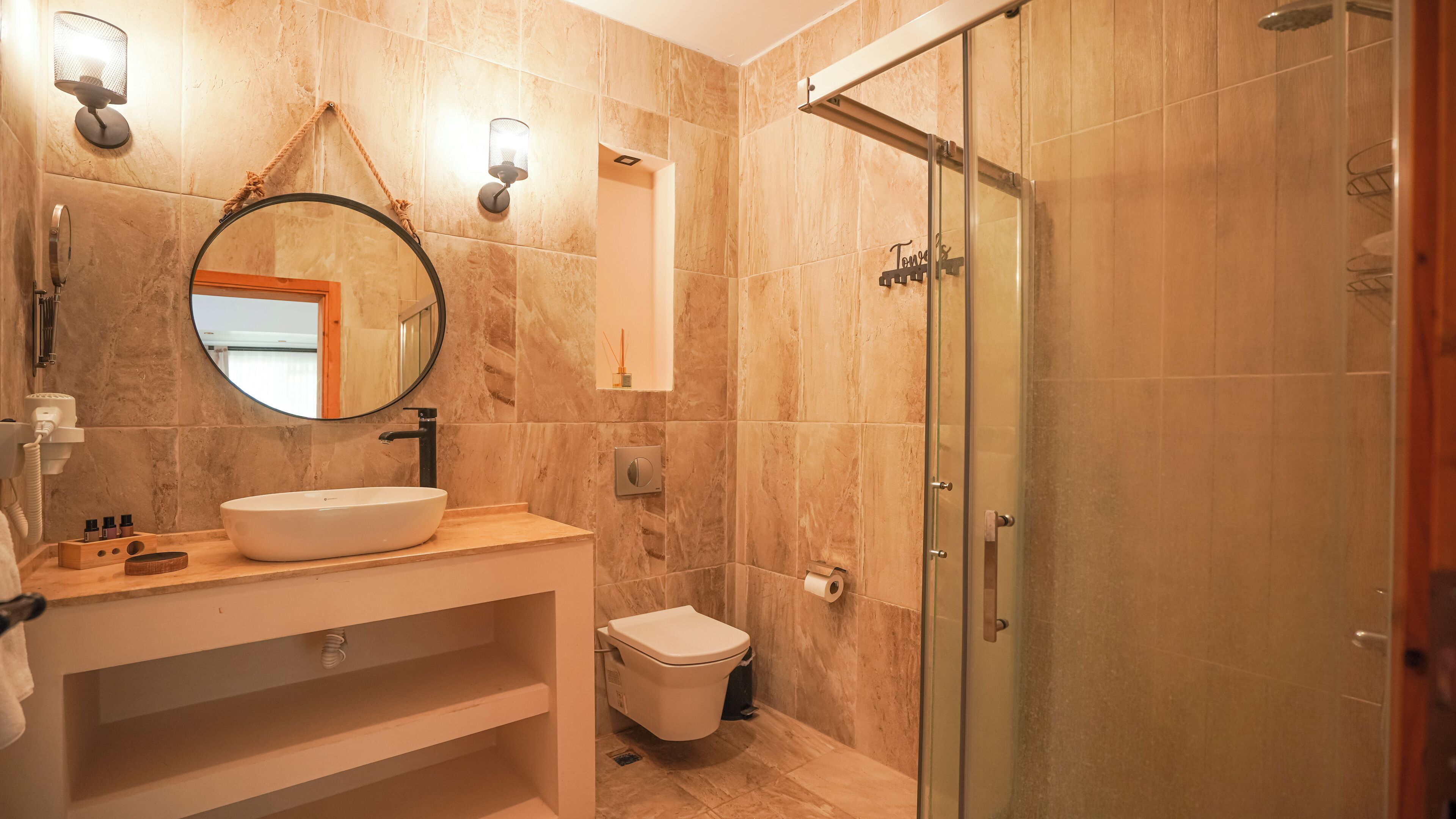 Une salle de bain avec un miroir rond, un lavabo, des toilettes et une douche à parois de verre.